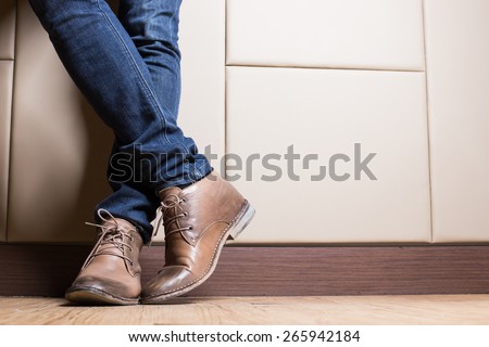 Young fashion man\'s legs in blue jeans and brown boots on wooden floor