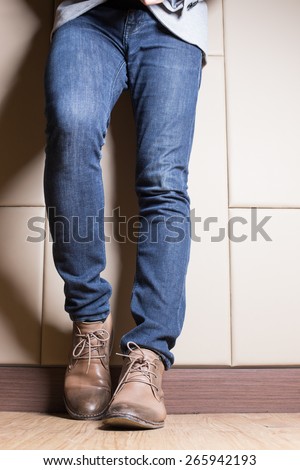 Young fashion man\'s legs in blue jeans and brown boots on wooden floor