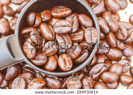 selective focus of coffee beans in spoon  on plank of wooden ,blurred background.