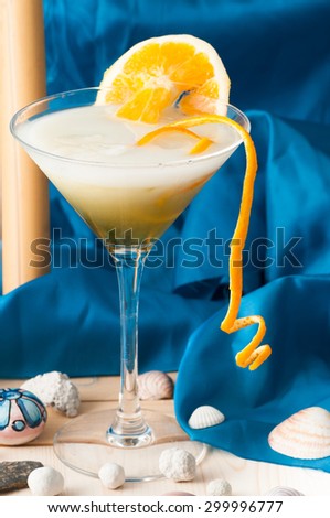 glass of alcoholic drink cocktail with orange slices, cubes and shaker rose on blue