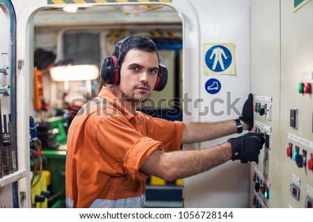 Marine engineer officer starts or stops main engine or generators of ship in engine room. Seamen\'s work. He wears ear protection.