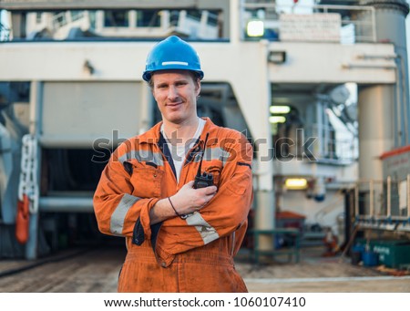 Marine Deck Officer or Chief mate on deck of offshore vessel or ship , wearing PPE personal protective equipment - helmet, coverall. He speaks to VHF walkie-talkie radio