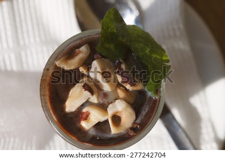 Hot chocolate with nuts in a transparent glass on a brown table. top view