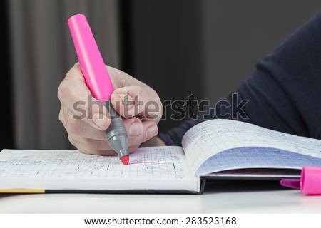 Female hand selects text pink marker in a student notebook. education