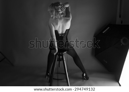 Full length black and white portrait of a beautiful model wearing a wonderful corset, in a photo studio near the spotlights