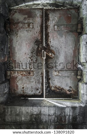 An old, rusting cast iron dungeon door letting in chinks of sunlight.