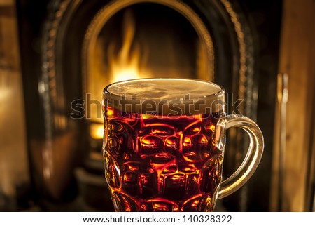 A pint of beer illuminated by a warming fire.