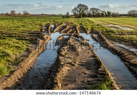 Deep tyre tracks made by a tractor  in a field filled with rain water.