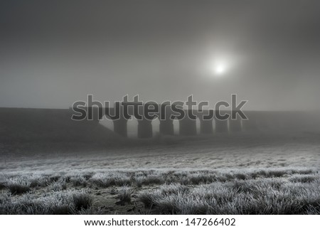 The Ribbehead Viaduct In Winter with train crossing and sun coming through fog making an atmospheric image.