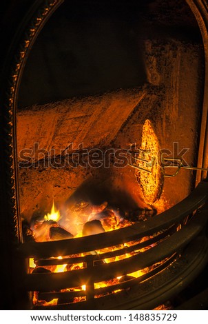 Bread being toasted by an open coal fire in Winter.