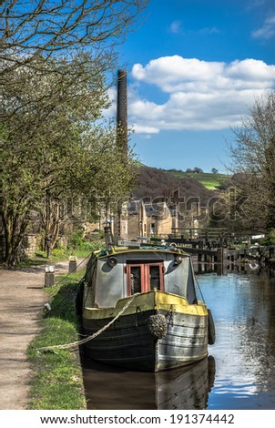 A narrow boat mored along the historic Rochdale canal near Todmorden  with old mill chimney in the background.
