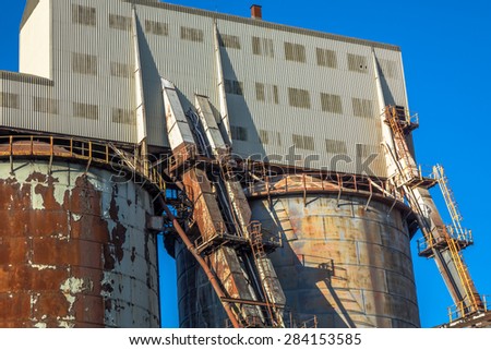 Industrial chemical plant tanks with old, rusting chutes.