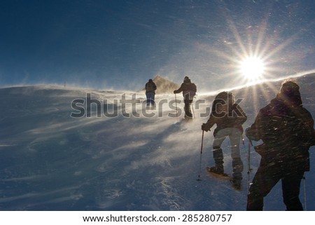 people hiking towards the top of the hill on the snow in a wind storm