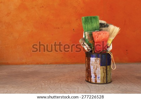 The old paint brush in rusty tin with space on orange cement wall