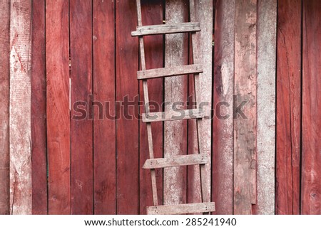 Vintage red tone wooden ladder with old wood wall background