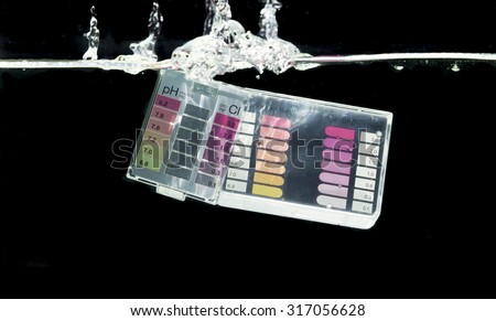 Swimming pool water testing kit dipping in water with black background