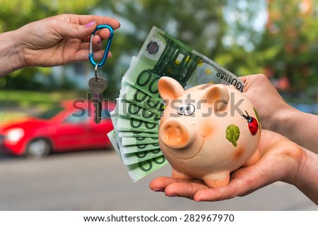Salesman giving car key to a new car owner, who is paying last saving money from piggy bank on blurred background