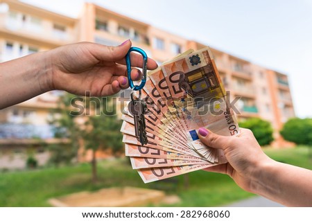 Real estate agent giving apartment keys to a new property owner, who is paying by euro money on blurred background