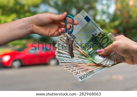 Salesman giving car key to a new car owner, who is paying by euro money on blurred background