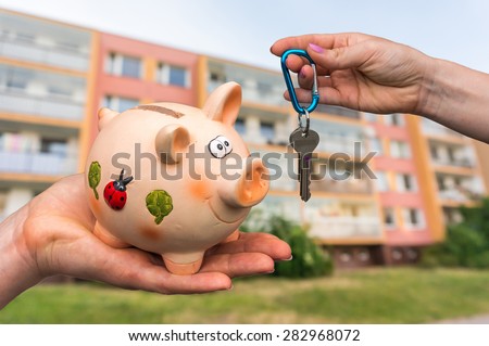 Real estate agent giving home keys to a new property owner, who is paying all saving money from piggy bank on blurred background