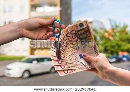 Real estate agent giving house keys to a new property owner, who is paying by euro money on blurred background