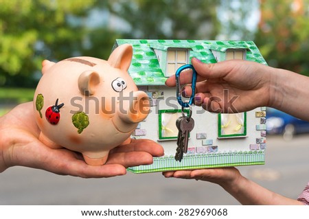 Real estate agent giving house keys to a new property owner, who is paying all saving money from piggy bank on blurred background