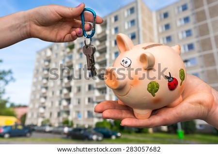 Real estate agent giving flat keys to a new property owner, who is paying last saving money from piggy bank on blurred background