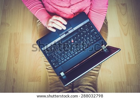 Young student using a laptop and sitting on the wooden floor in a classroom - retro and vintage style
