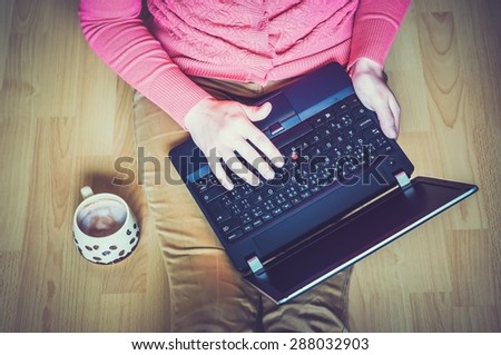 Young student using a laptop and sitting on the wooden floor in a classroom - retro and vintage style