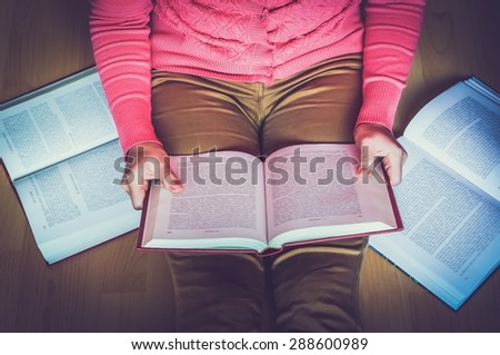 Young woman on the wooden floor in the library reading a book, studying - retro and vintage style