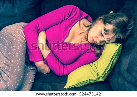 Woman lying on sofa and holding hands on her stomach at home - retro style