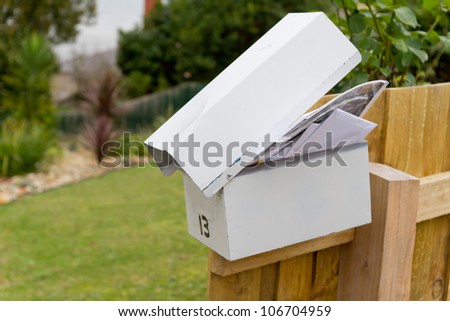 Overflowing full white metal letterbox on fence post