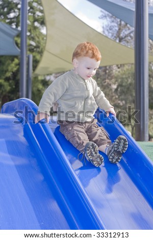 Boy sliding down slide with playground background