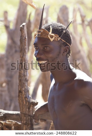 DAMARALAND, NAMIBIA, SOUTH AFRICA. 30 MARCH 2012: Portrait of a young black man of African Damara tribe in typical African ornaments on the head smiles and looks into the distance. Naked with muscles