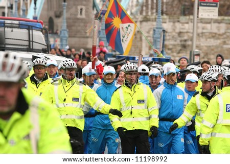 Olympic Torch relay for 2008 Beijing Olympics crossing London\'s Tower Bridge. Runner protected by police escort in case of protest