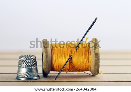 Old spool of thread with needle closeup.  Tailor\'s work table. textile or fine cloth making.