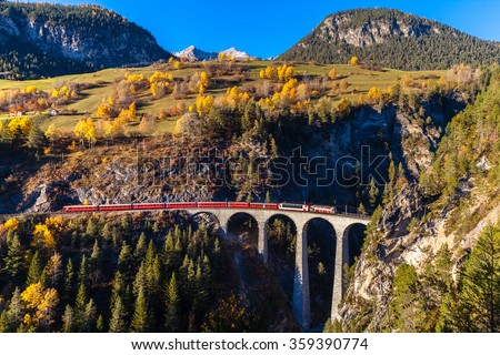 The train of  Rhaetian Railway running on the famous Landwasser Viaduct into the tunnel, with view of colorful trees on a sunny autumn day, Canton of Grisons, Switzerland