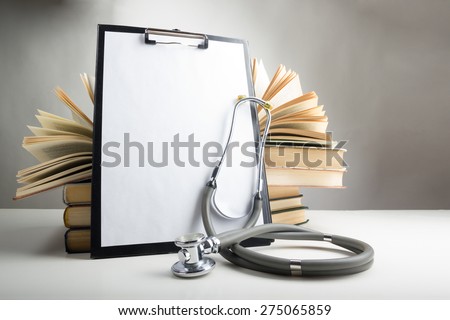 Open hardback books on the table, medical clipboard with blank paper (document, report) and stethoscope. Medical professional education and information concept. Back to school, copy space.