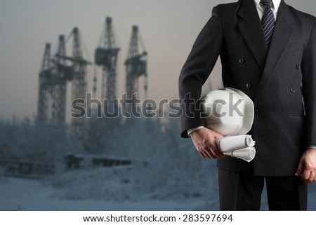 Architect hand holding white safety helmet for workers security and blueprints standing in front of blurred urban background.