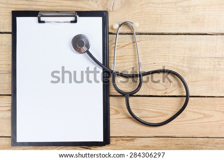 Medical clipboard and stethoscope on wooden desk background. Top view. Workplace of a doctor.