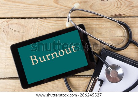 Burnout - Workplace of a doctor. Tablet, stethoscope, clipboard on wooden desk background. Top view