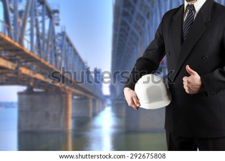 Close up of engineer hand holding white safety helmet for workers security standing in front of  blurred construction site in background