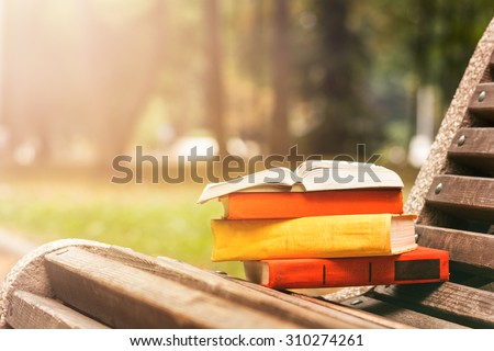 Stack of hardback book and Open book lying on a bench at sunset  park on blurred nature  backdrop. Copy space, back to school. Education background.