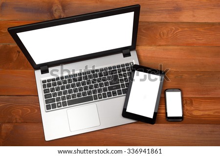 Set of modern gadgets includes laptop, digital tablet and smartphone with empty white screen on wooden table. Top view