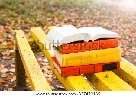 Stack of hardback book and Open book lying on a bench at sunset park on blurred nature backdrop. Copy space, back to school. Education background.