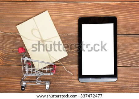 Online shopping concept - Empty Shopping Cart, tablet pc, gift box on rustic wooden background. Top view. Copy space for text.