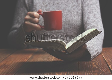 Young woman reading a book and holding cup of tea or coffee. Toned image