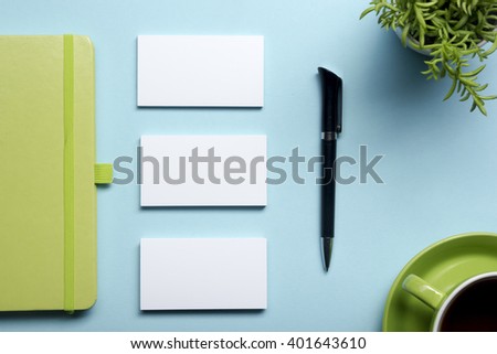 Business card blank, notepad, flower, coffee cup and pen at office desk table top view. Corporate stationery branding mock-up