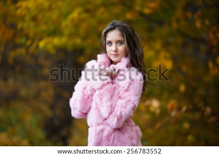 Portrait of beautiful girl in a pink fur coat on a background of yellow leaves