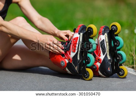 Young girl sitting on the ground and putting on inline skates